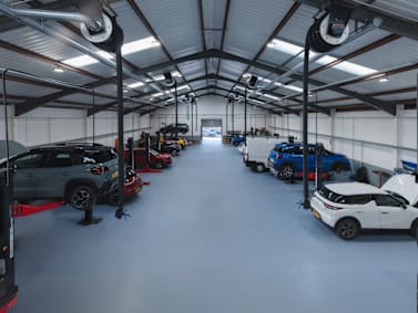 Cars in a garage workshop, with several vehicles on hydraulic lifts.